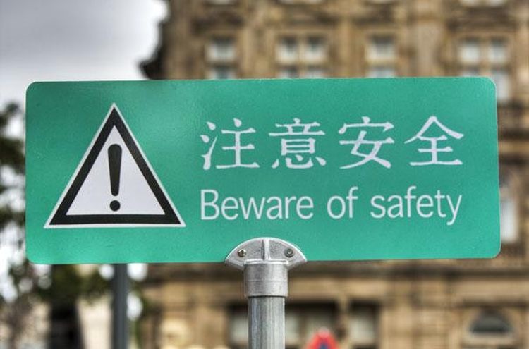 A green sign mounted on a pole with the hazard alert triangle and exclamation point, followed by a line of Chinese text and a line of English text reading "Beware of Safety"