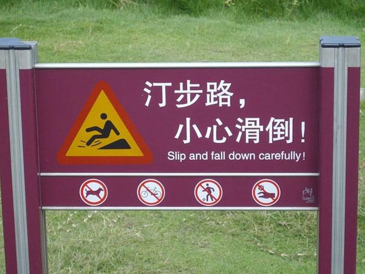 I shot this photo when I was in Japan a few years ago because the translation made me laugh. A purple sign with white lettering and the hazard alert triangle outlined in red with a slip and fall graphic inside. There are two lines of Japanes text, with a line of English text below reading "Slip and fall down carefully."